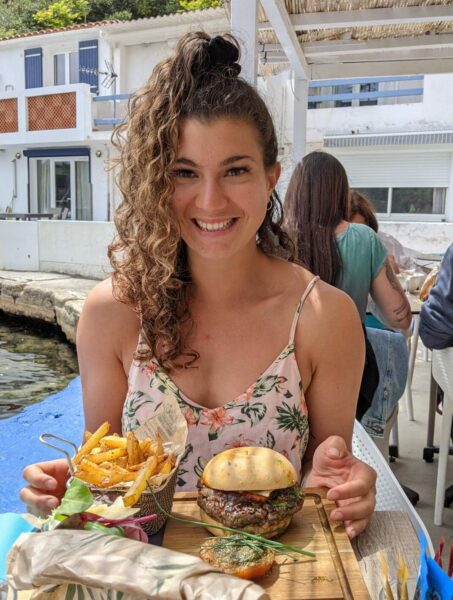 June, souriante, mange un burger et des frites à la terrasse d'un restaurant.