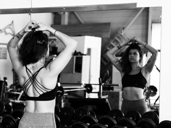 June se trouve face à un miroir dans une salle de musculation. Elle refait son chignon, déterminée à poursuivre l'entraînement.